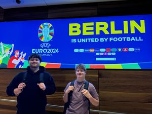 Ben and Ian in front of a UEFA Euro Fanzone advertisement at the Brandenburg Airport